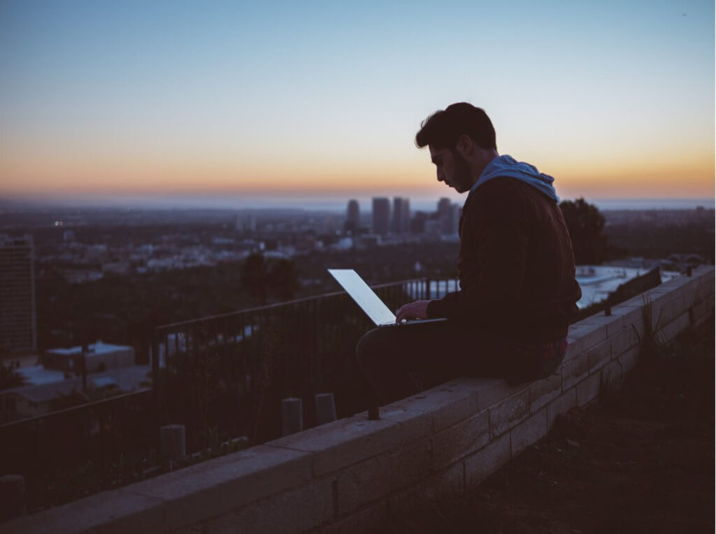 Boy sitting in top of a building carrying a laptop and working remotely